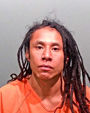 A man with long dreadlocks is shown in a mugshot wearing an orange jumpsuit.