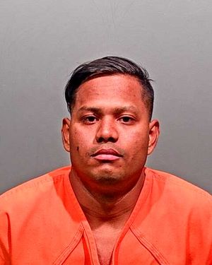 A man wearing an orange jumpsuit poses for a mugshot against a plain background.